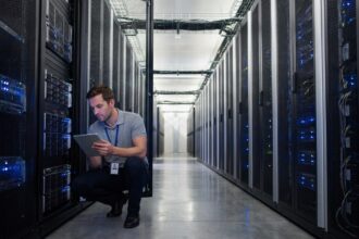 Technicien inspectant des serveurs dans un couloir de centre de données moderne avec des rangées de racks illuminés par des voyants LED bleus